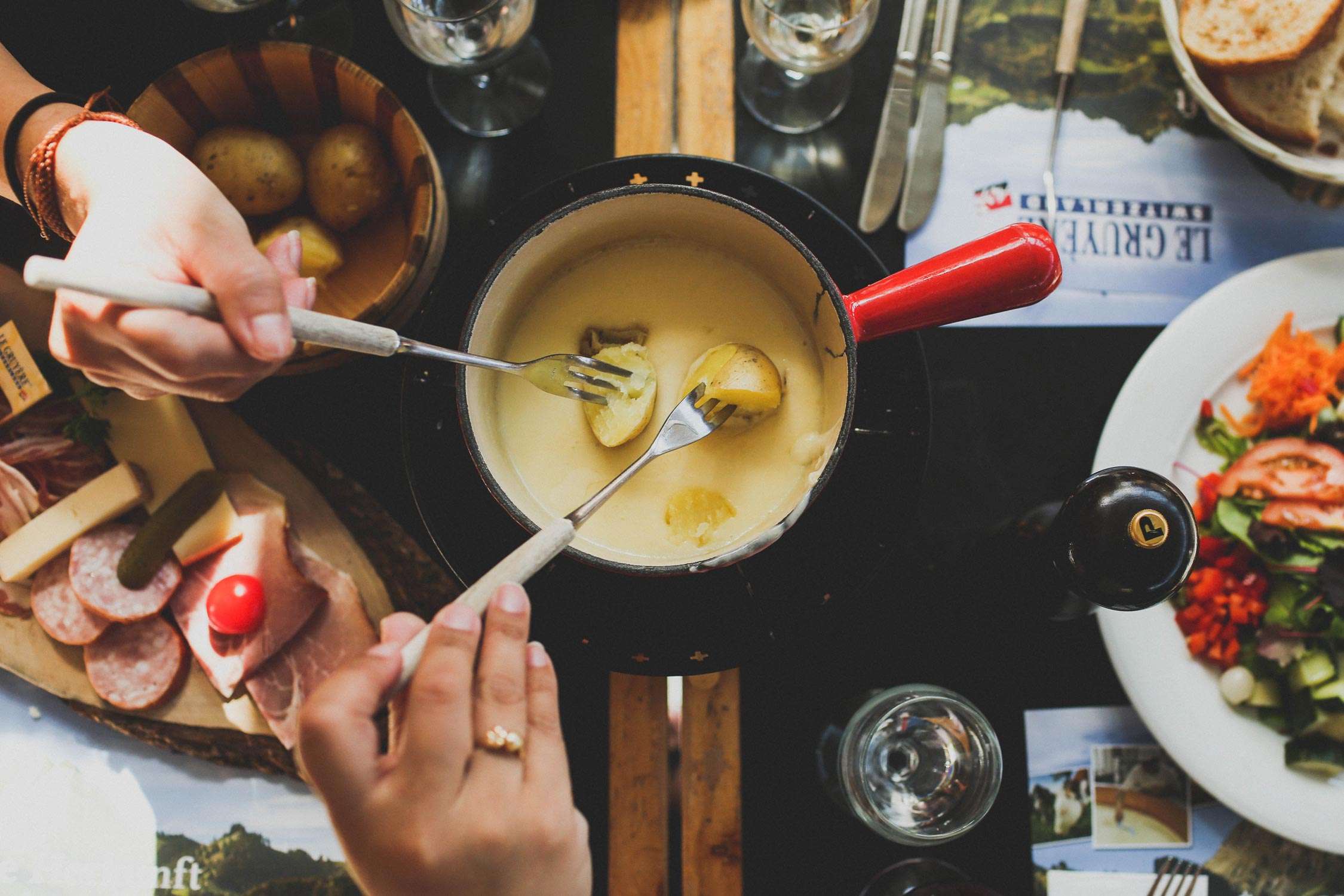 Two people holding forks are dipping food into the fondue.
