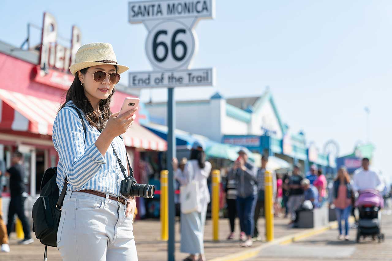 Chinese tourist surfs the internet with her smartphone at the Santa Monica Pier, near the end of Route 66 sign