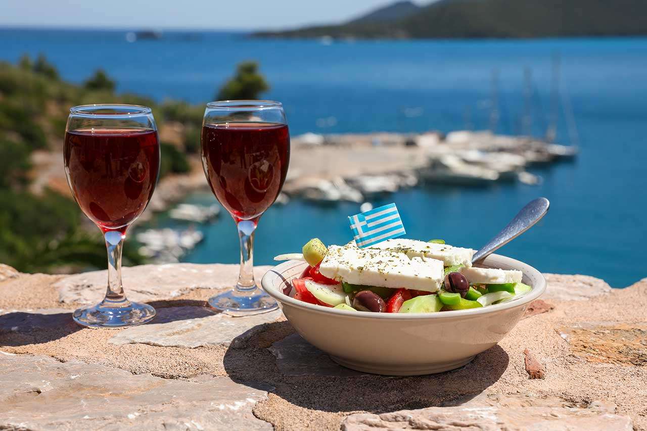 Two glasses of red wine and bowl of greek salad by the sea view