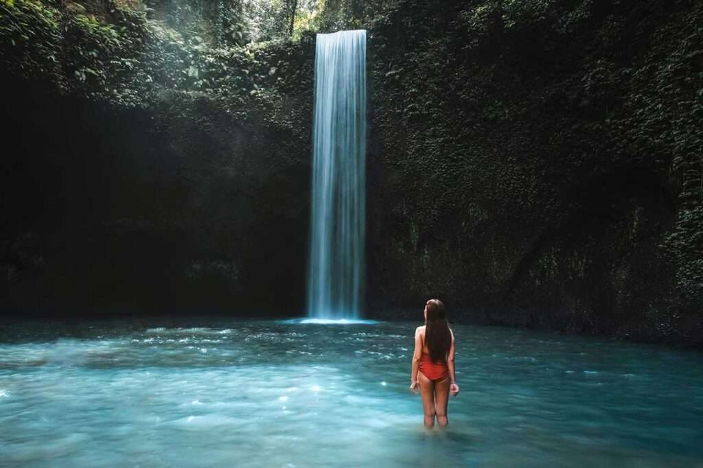 Traveling woman with tropical rainforest in Bali enjoying life at beautiful Tibumana waterfall.