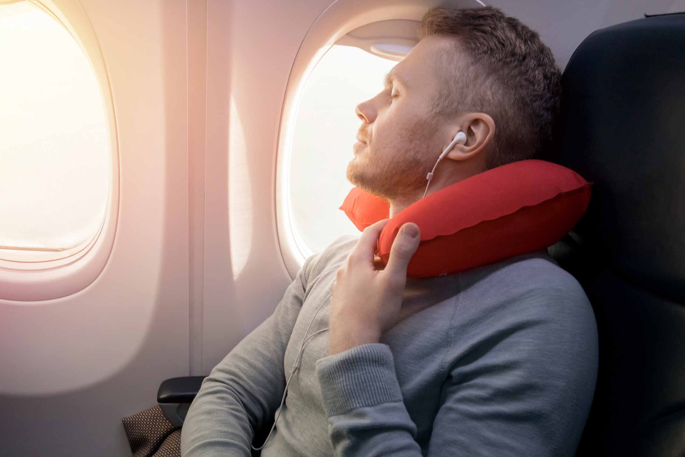 Male passenger of airplane listens to music and enjoys pillow for sleeping in chair