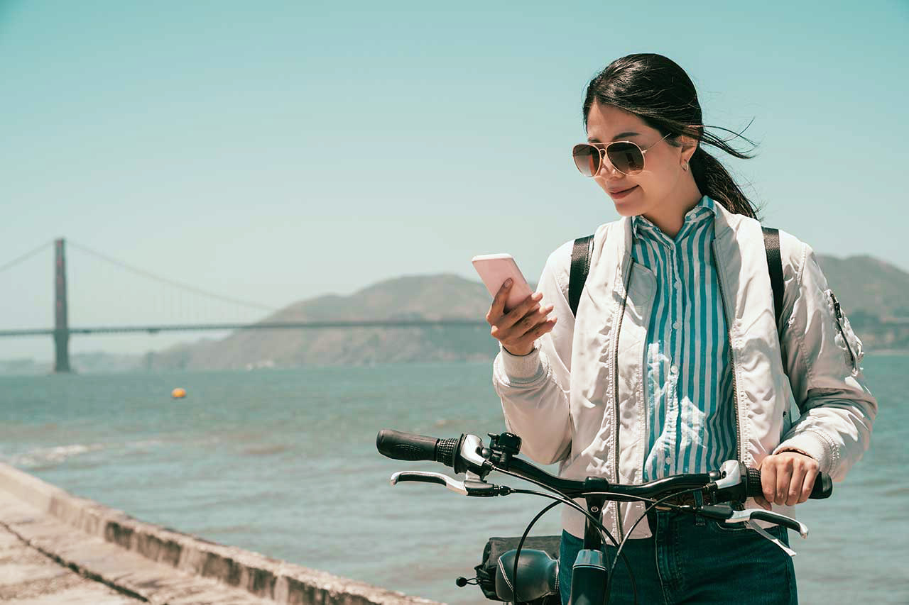 Girl traveler walk with bike using digital travel guide on mobile phone