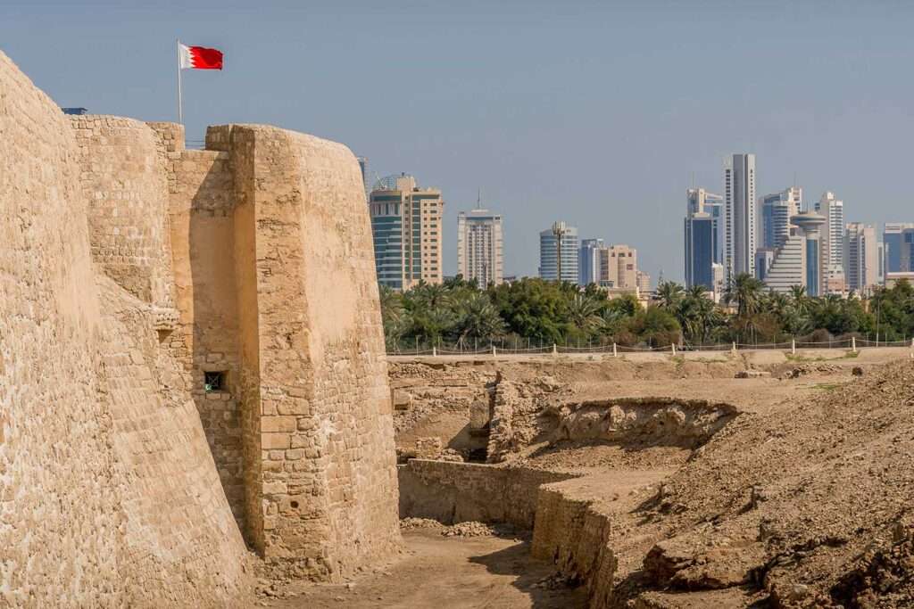 The UNESCO site of Qal'at al-Bahrain in Manama, with the city skyline and the Bahraini flag 