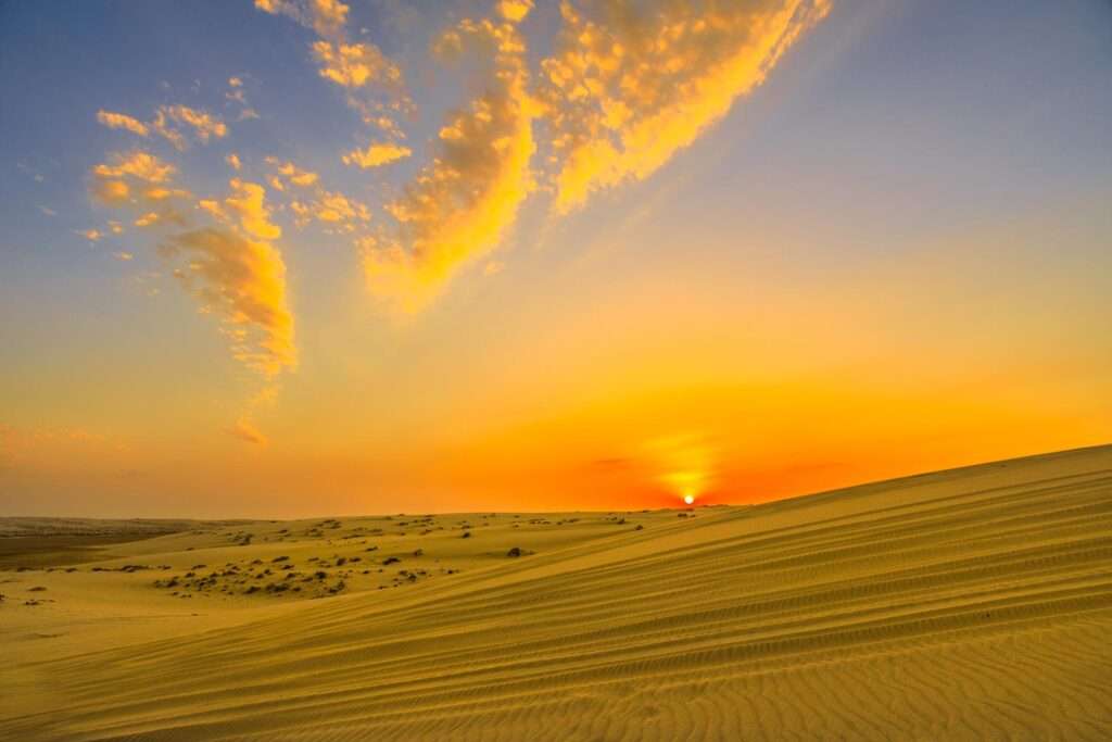 Sun at sunset over desert sand dunes at Khor Al Udeid (Inland Sea) in Qatar.