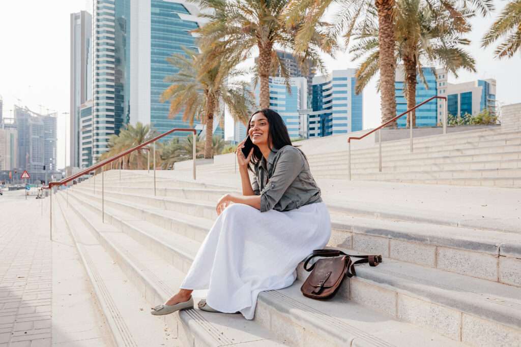 Young Indian woman smiling talking on smartphone, seating on stairs in Doha, Qatar